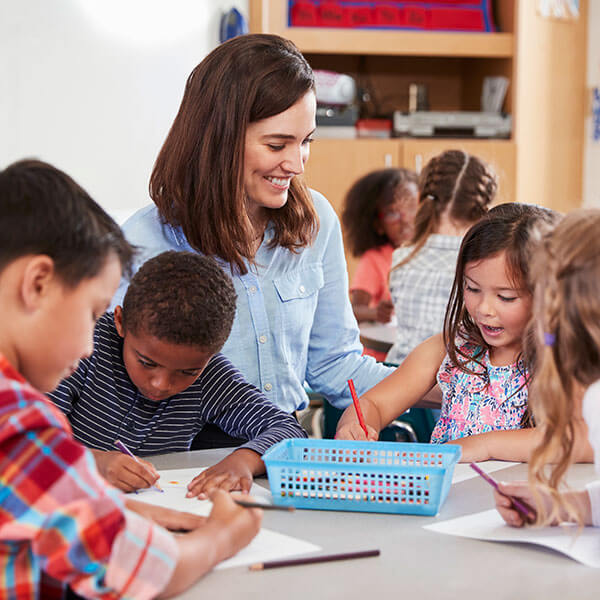 teacher helping young children color at table