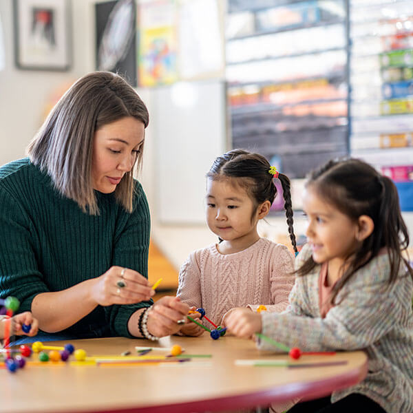 teacher helping young girls play at table
